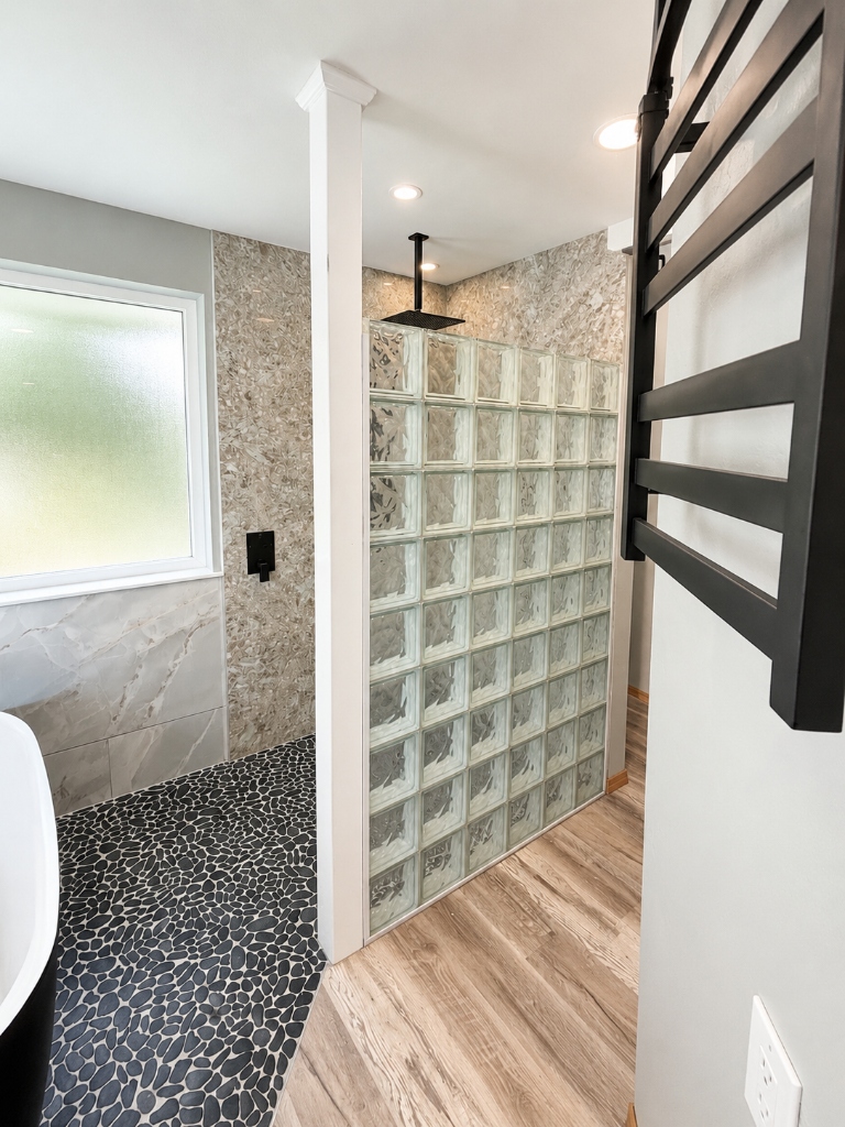 Walk-in shower with glass block wall, black pebble tile floor and matte black rain shower head in Kitsap County, WA